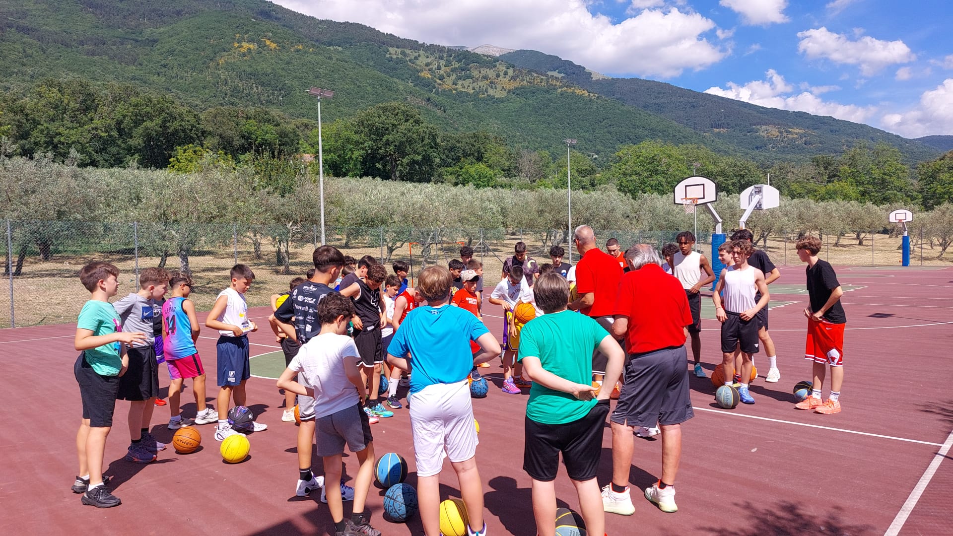 Bambini e ragazzi con i palloni durante un allenamento di basket all’aperto